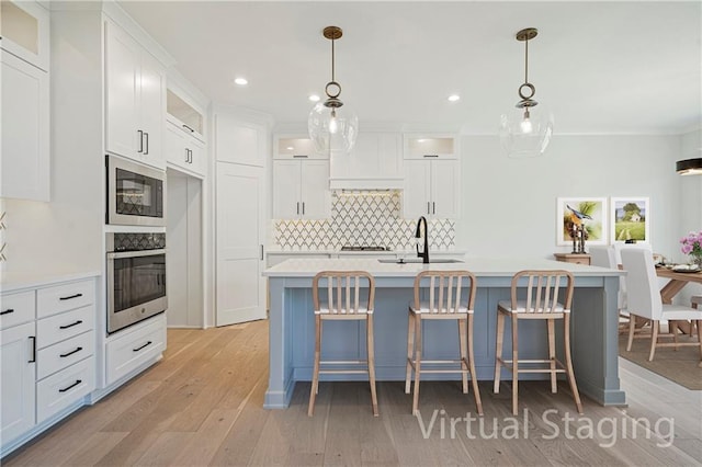 kitchen featuring a kitchen island with sink, hanging light fixtures, white cabinetry, and stainless steel oven