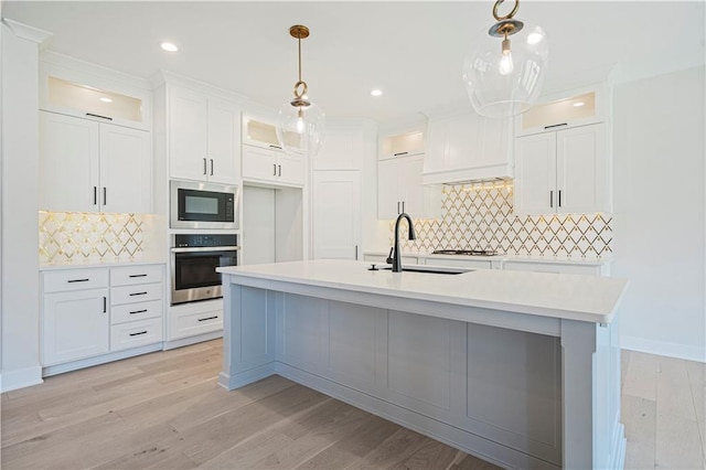 kitchen with sink, a kitchen island with sink, built in microwave, decorative light fixtures, and stainless steel oven