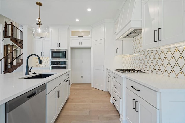 kitchen with premium range hood, pendant lighting, sink, white cabinets, and stainless steel appliances