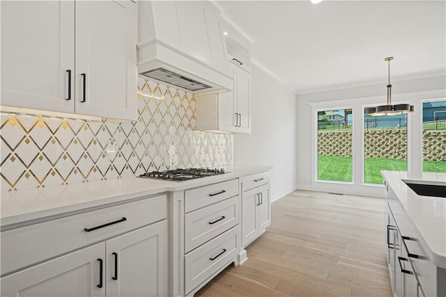 kitchen featuring decorative light fixtures, white cabinets, decorative backsplash, ornamental molding, and custom range hood