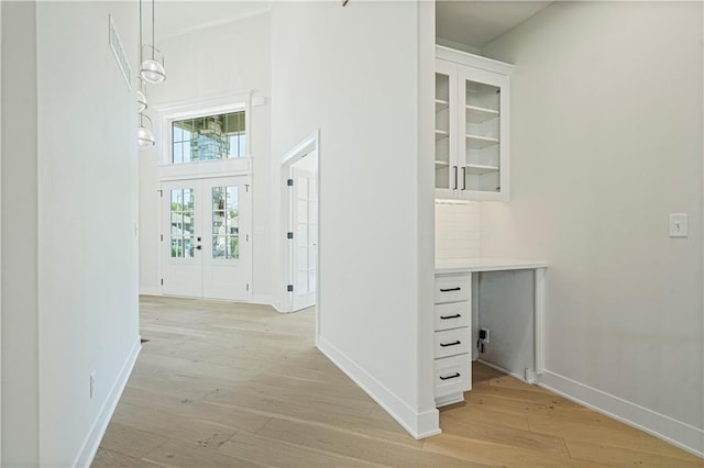 corridor with french doors, a high ceiling, and light wood-type flooring