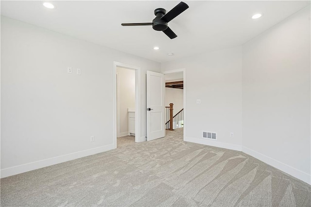 unfurnished bedroom with ceiling fan, a walk in closet, ensuite bath, and light carpet