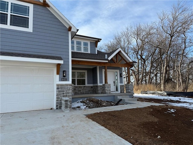 view of front facade featuring covered porch, a garage, a shingled roof, stone siding, and driveway