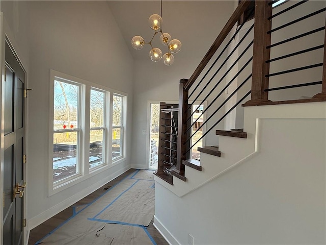 foyer entrance with an inviting chandelier, wood finished floors, high vaulted ceiling, baseboards, and stairs