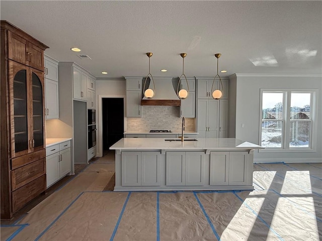 kitchen with gray cabinets, pendant lighting, sink, custom range hood, and a center island with sink