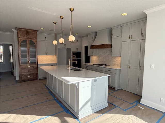 kitchen with an island with sink, custom range hood, gray cabinets, gas cooktop, and a sink