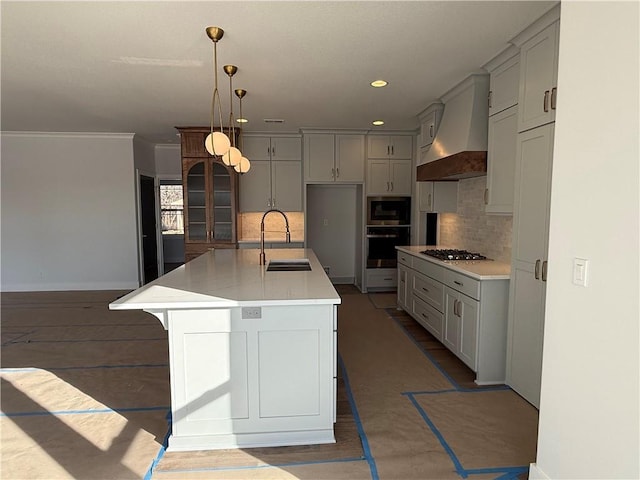 kitchen featuring sink, appliances with stainless steel finishes, a kitchen island with sink, premium range hood, and decorative light fixtures