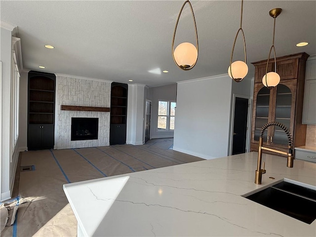 kitchen featuring sink, a fireplace, ornamental molding, light stone countertops, and decorative light fixtures