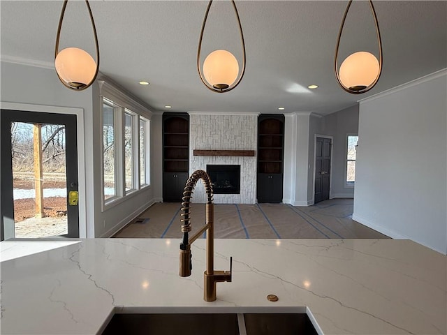 kitchen with sink, crown molding, a stone fireplace, and decorative light fixtures