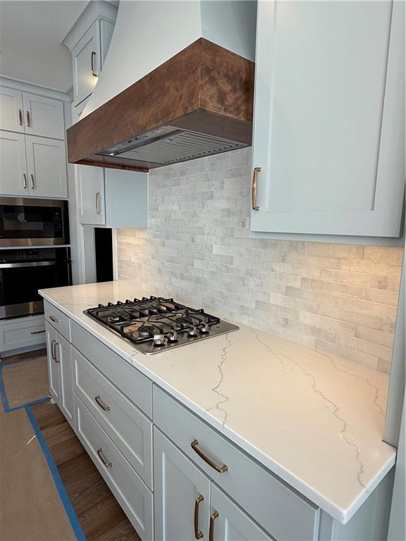 kitchen featuring tasteful backsplash, custom range hood, appliances with stainless steel finishes, and light stone counters