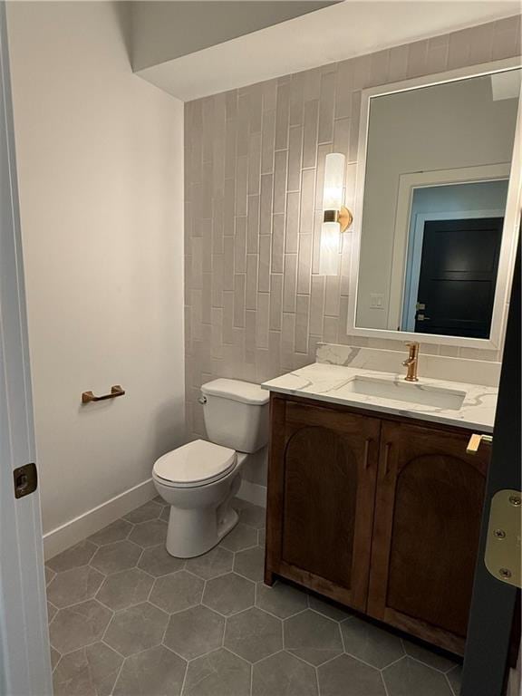 half bath with toilet, baseboards, vanity, and tile patterned floors