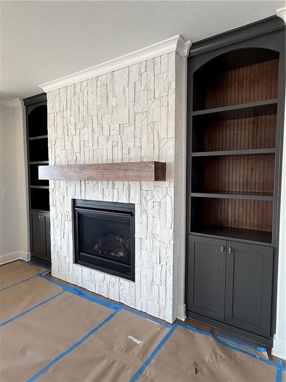 unfurnished living room with crown molding, a textured ceiling, built in features, and a fireplace