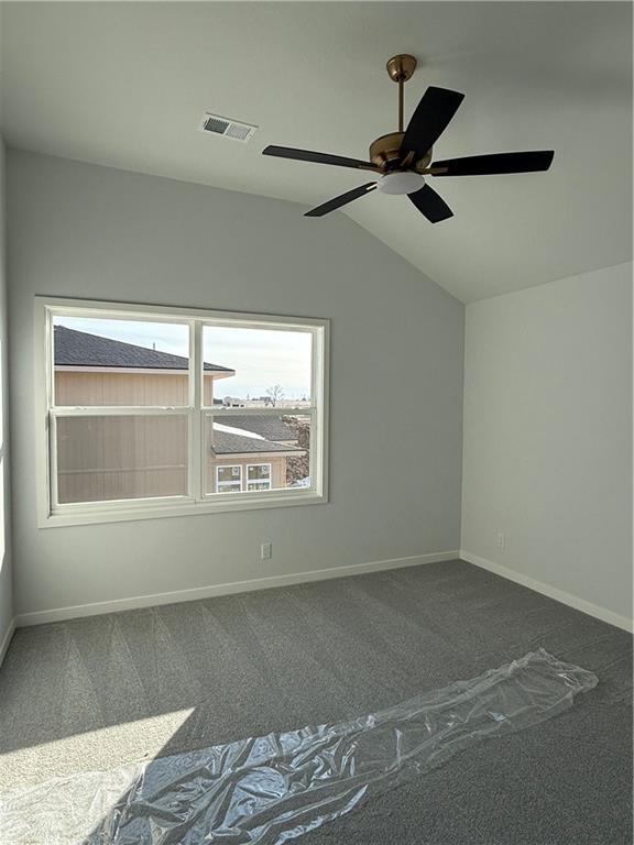 carpeted empty room featuring visible vents, vaulted ceiling, baseboards, and ceiling fan