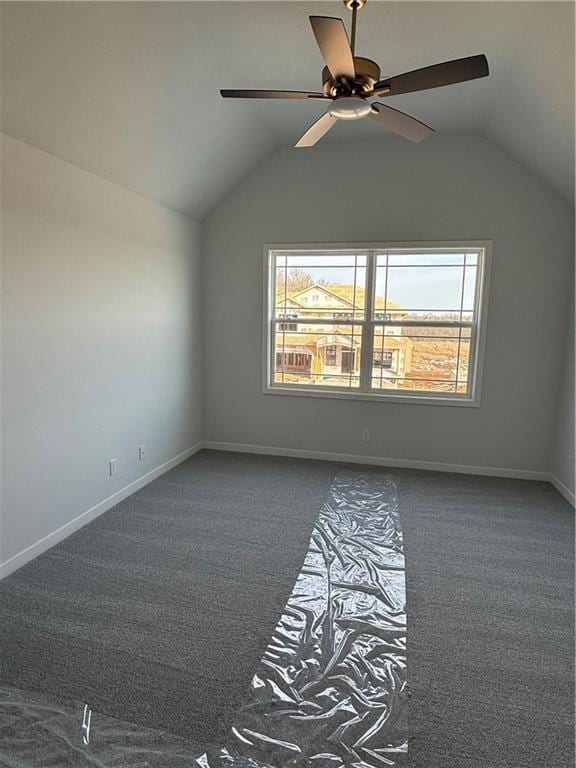 unfurnished room featuring lofted ceiling, dark carpet, and baseboards