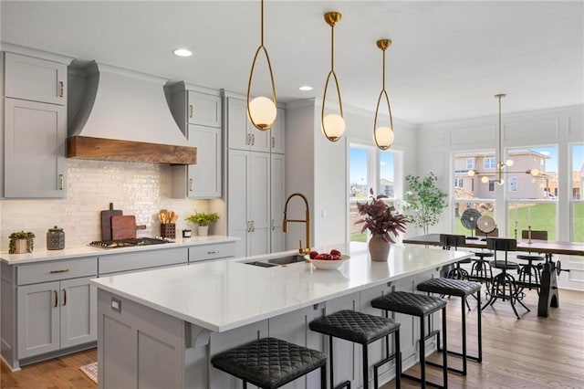 18452 Windsor St, Overland Park, KS 66085 - kitchen featuring stainless steel gas stovetop, light countertops, a sink, a center island with sink, and custom range hood