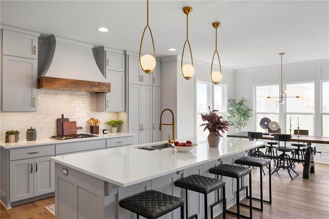 18452 Windsor St, Overland Park, KS 66085 - kitchen with stainless steel gas cooktop, decorative backsplash, custom range hood, light countertops, and an island with sink