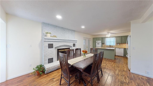 dining room featuring a fireplace, sink, dark wood-type flooring, and ceiling fan