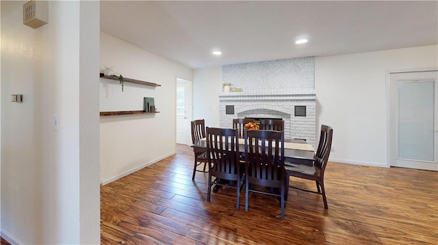 dining area with dark wood-type flooring and a brick fireplace