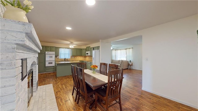 dining area featuring a fireplace, ceiling fan, sink, and dark hardwood / wood-style floors