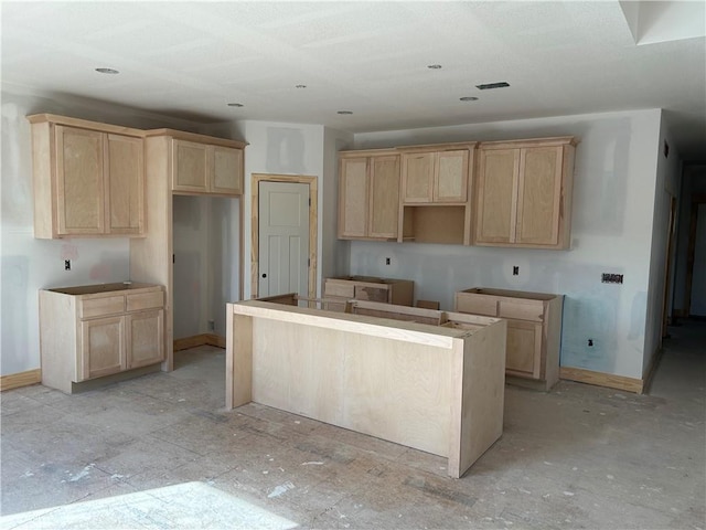 kitchen with light brown cabinetry, a kitchen island, and baseboards