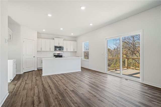 kitchen featuring white cabinets, a center island with sink, backsplash, appliances with stainless steel finishes, and dark hardwood / wood-style floors