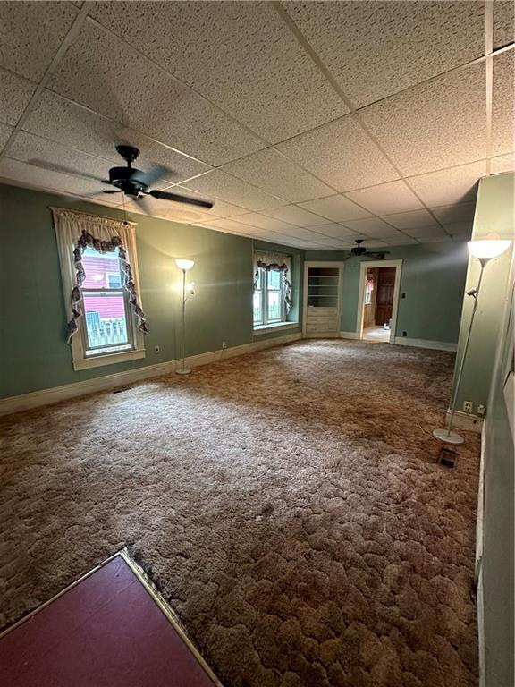 carpeted empty room with ceiling fan and a drop ceiling