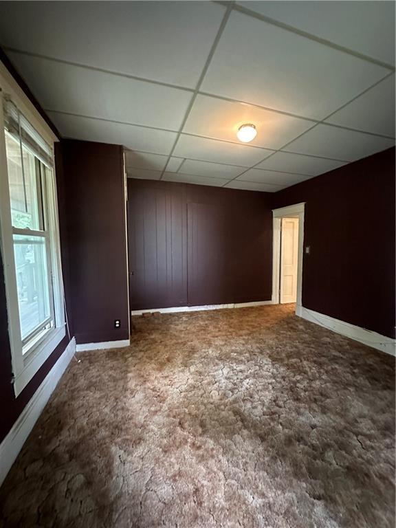 unfurnished room with dark carpet, a paneled ceiling, and wood walls