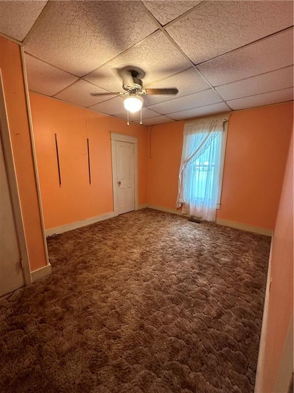 carpeted empty room featuring ceiling fan and a drop ceiling