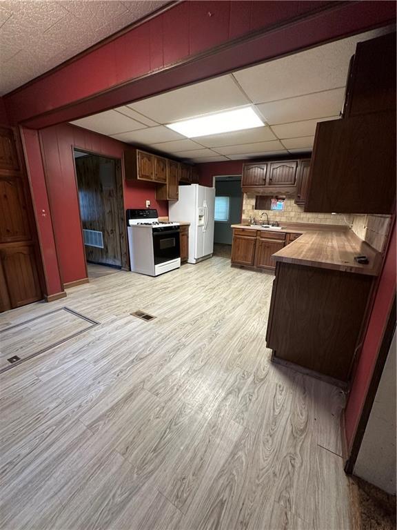 kitchen featuring white appliances, light hardwood / wood-style flooring, sink, a drop ceiling, and tasteful backsplash