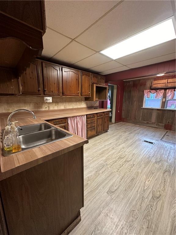 kitchen with sink, a drop ceiling, wooden counters, wood walls, and light hardwood / wood-style floors