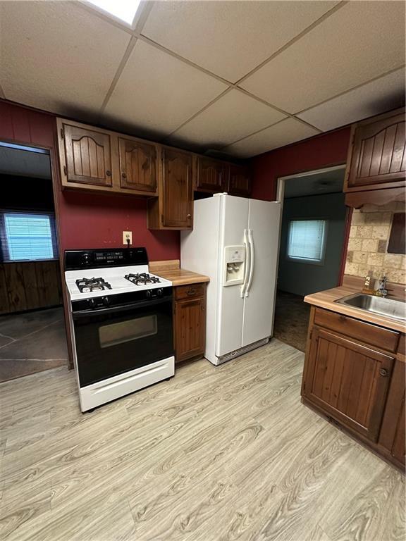 kitchen with range with gas cooktop, light hardwood / wood-style floors, white refrigerator with ice dispenser, sink, and a paneled ceiling