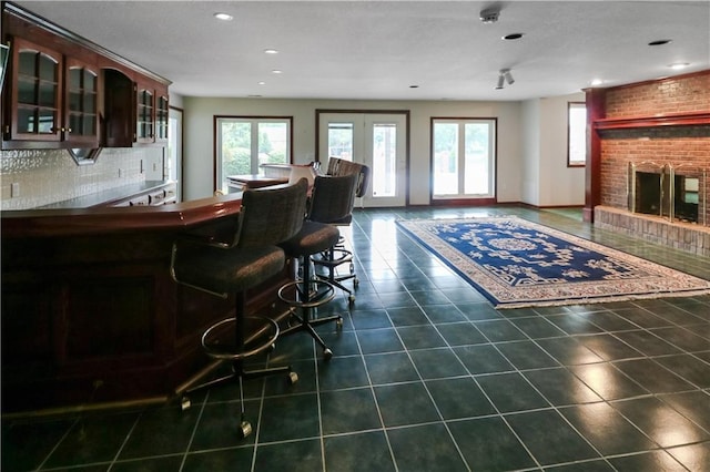 interior space featuring tasteful backsplash, dark tile patterned flooring, glass insert cabinets, dark brown cabinets, and a fireplace