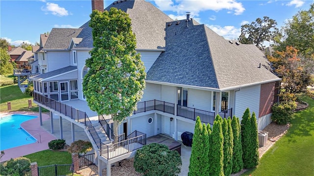 rear view of property featuring a fenced in pool, a patio, a sunroom, roof with shingles, and stairs