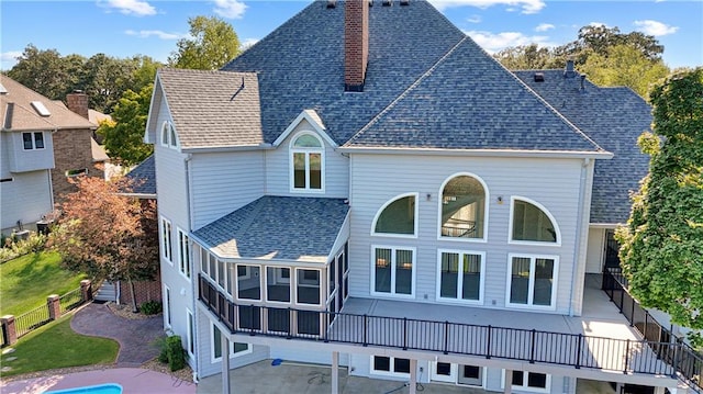 rear view of property with a shingled roof, a chimney, fence, and a lawn