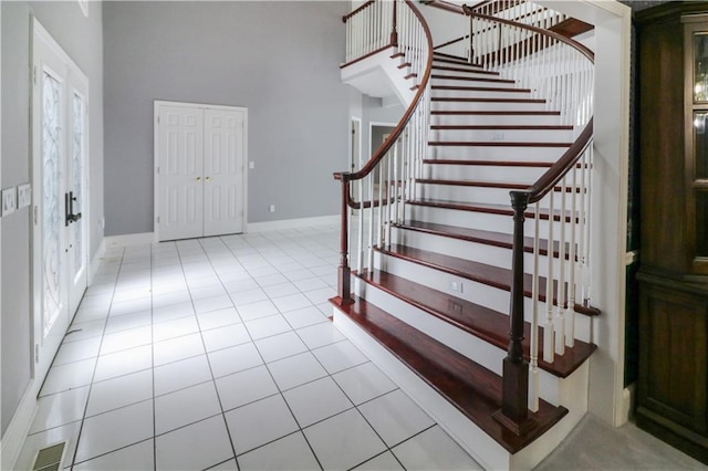 tiled foyer entrance with a high ceiling, stairway, visible vents, and baseboards