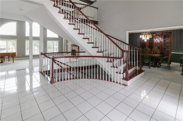 stairs with a chandelier, a high ceiling, carpet flooring, tile patterned floors, and decorative columns