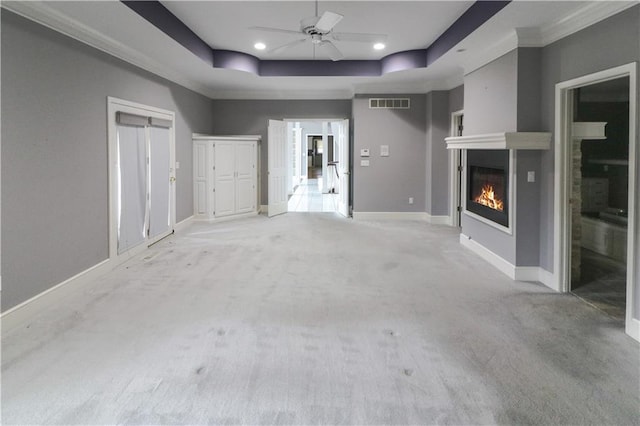 unfurnished living room featuring light colored carpet, ceiling fan, ornamental molding, and a tray ceiling