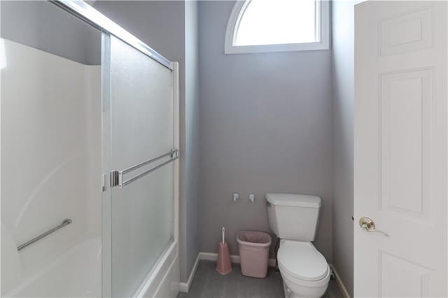 bathroom with baseboards, toilet, and bath / shower combo with glass door