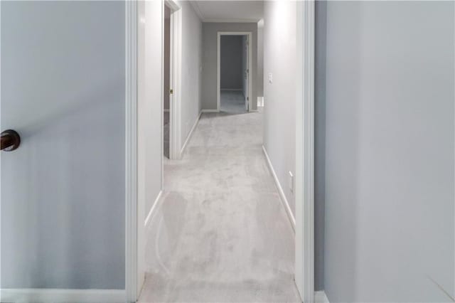 hallway with baseboards, ornamental molding, and light colored carpet