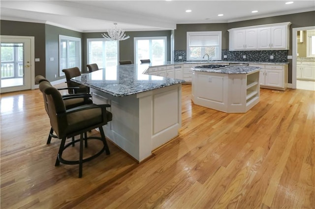 kitchen with a breakfast bar, a kitchen island, white cabinetry, backsplash, and light wood finished floors