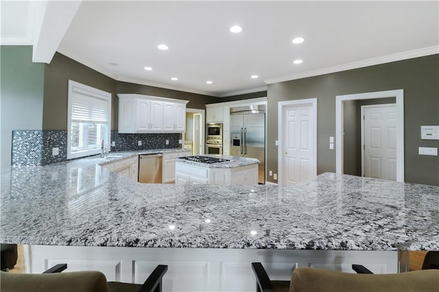 kitchen with light stone counters, tasteful backsplash, a sink, built in appliances, and a peninsula