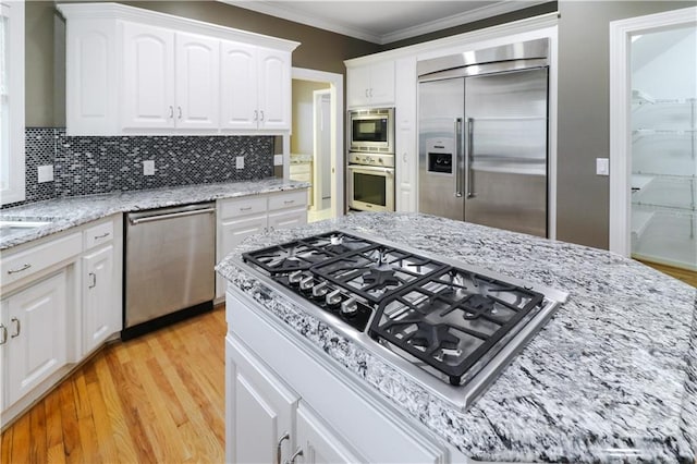 kitchen with built in appliances, white cabinetry, ornamental molding, light wood-type flooring, and decorative backsplash