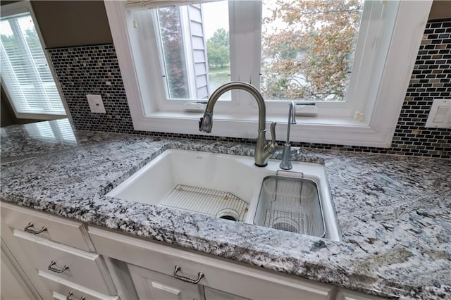 details with sink, light stone countertops, and white cabinetry