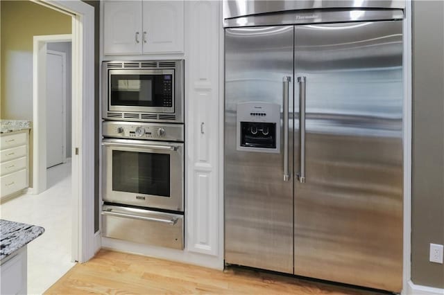 kitchen with built in appliances, light stone counters, light hardwood / wood-style floors, and white cabinets