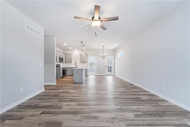 unfurnished living room featuring hardwood / wood-style flooring, sink, and ceiling fan with notable chandelier