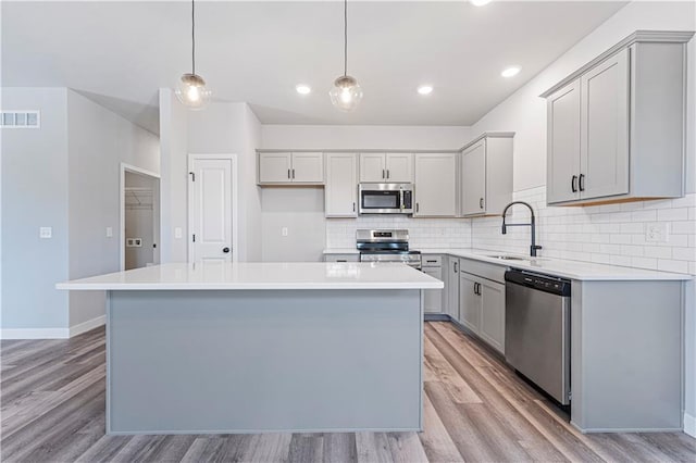 kitchen with pendant lighting, sink, gray cabinets, appliances with stainless steel finishes, and a kitchen island