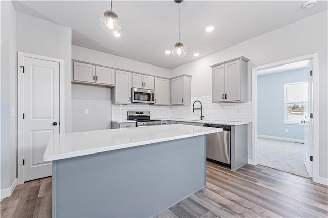 kitchen with light hardwood / wood-style flooring, appliances with stainless steel finishes, gray cabinetry, hanging light fixtures, and a kitchen island