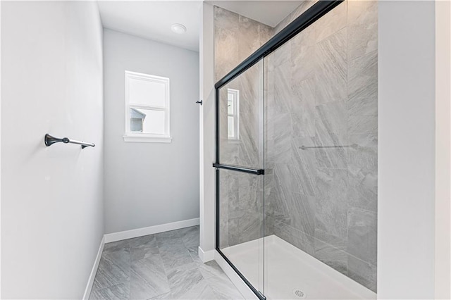 bathroom with marble finish floor, a shower stall, and baseboards