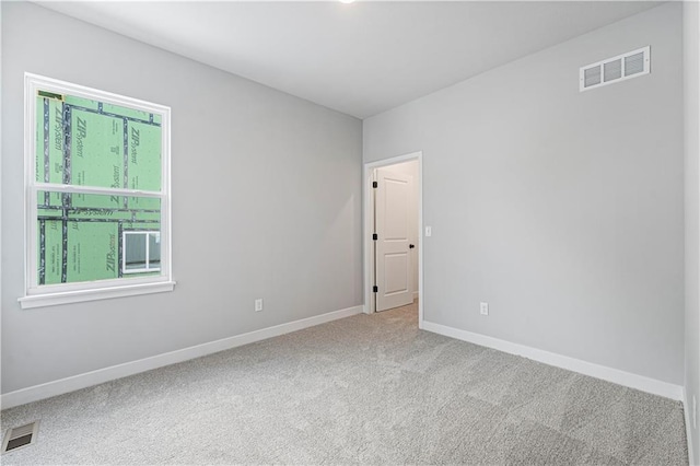 empty room with carpet floors, a wealth of natural light, visible vents, and baseboards