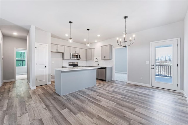 kitchen with light wood-style flooring, a sink, light countertops, appliances with stainless steel finishes, and decorative backsplash